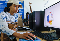 female student looking at a computer with her hand on the mouse in a classroom.