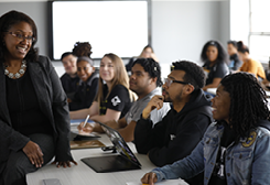 students looking up at a teacher in a classroom as the teacher smiles at them.