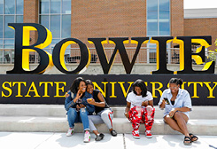 female students sitting at bowie state university sign on campus