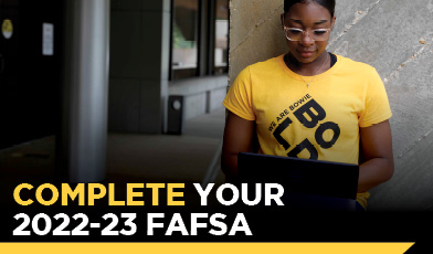 women student wearing a yellow shit on computer. text: complete your 2022-23 FAFSA