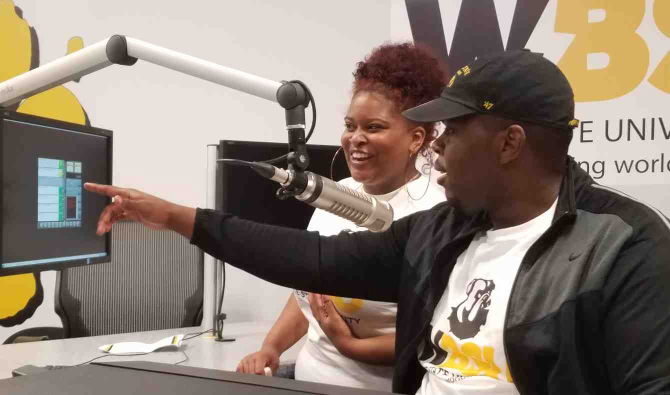 Two students in the WBSU Radio Station are sitting in front of a hanging microphone