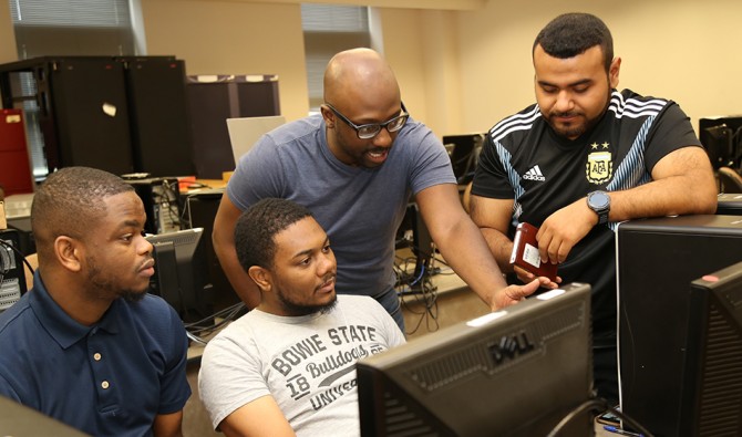 Four male students gather around a computer screen
